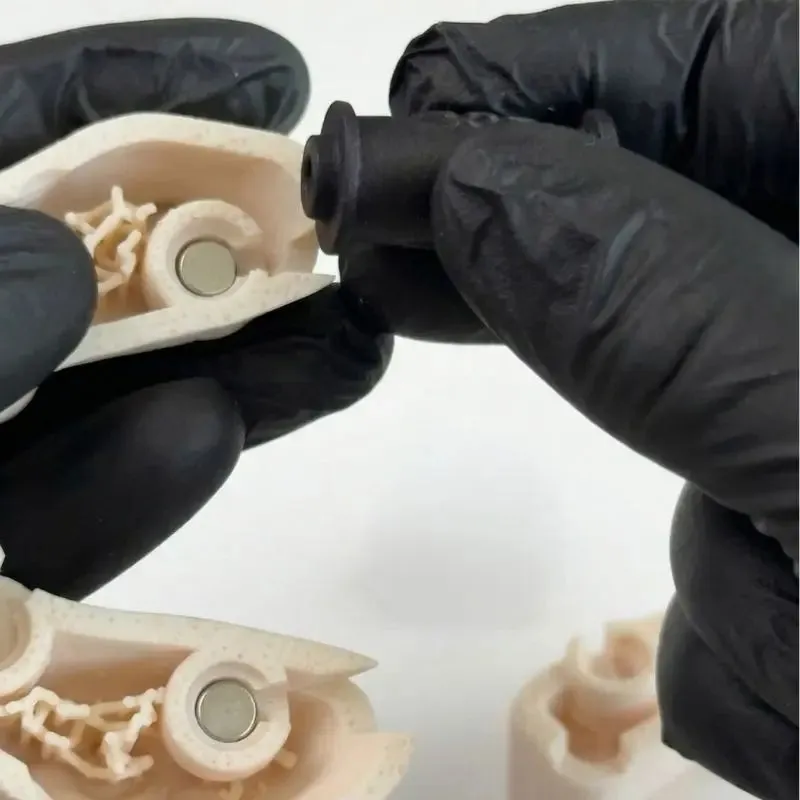Mains gantées mettant en place un aimant dans un modèle imprimé avec l’Omni GlueJet™