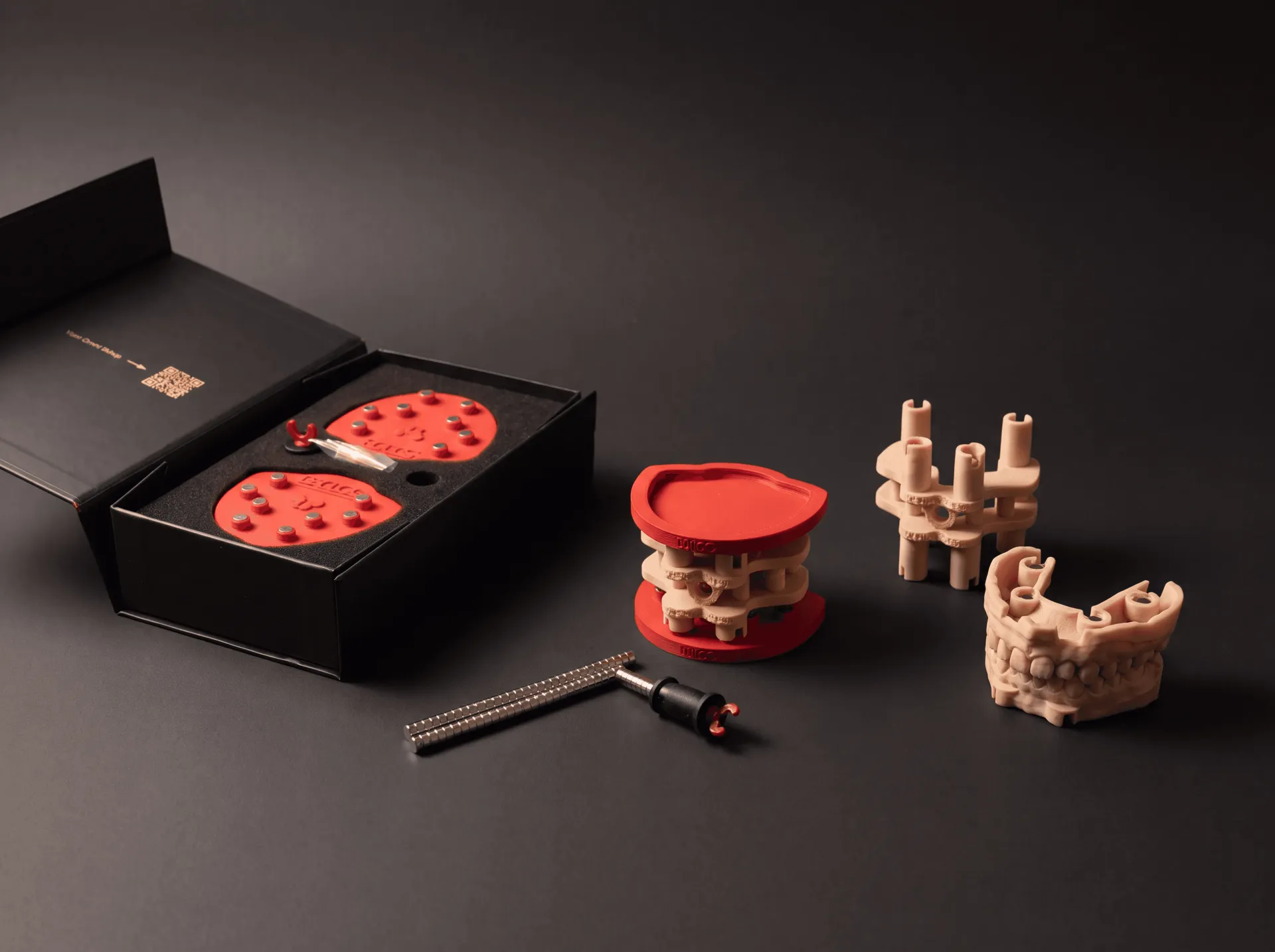 The DACOS Omni kit unboxed: red plates in the open box, the Omni GlueJet™ tool, a printed calibrator between two plates and printed models with magnet seats