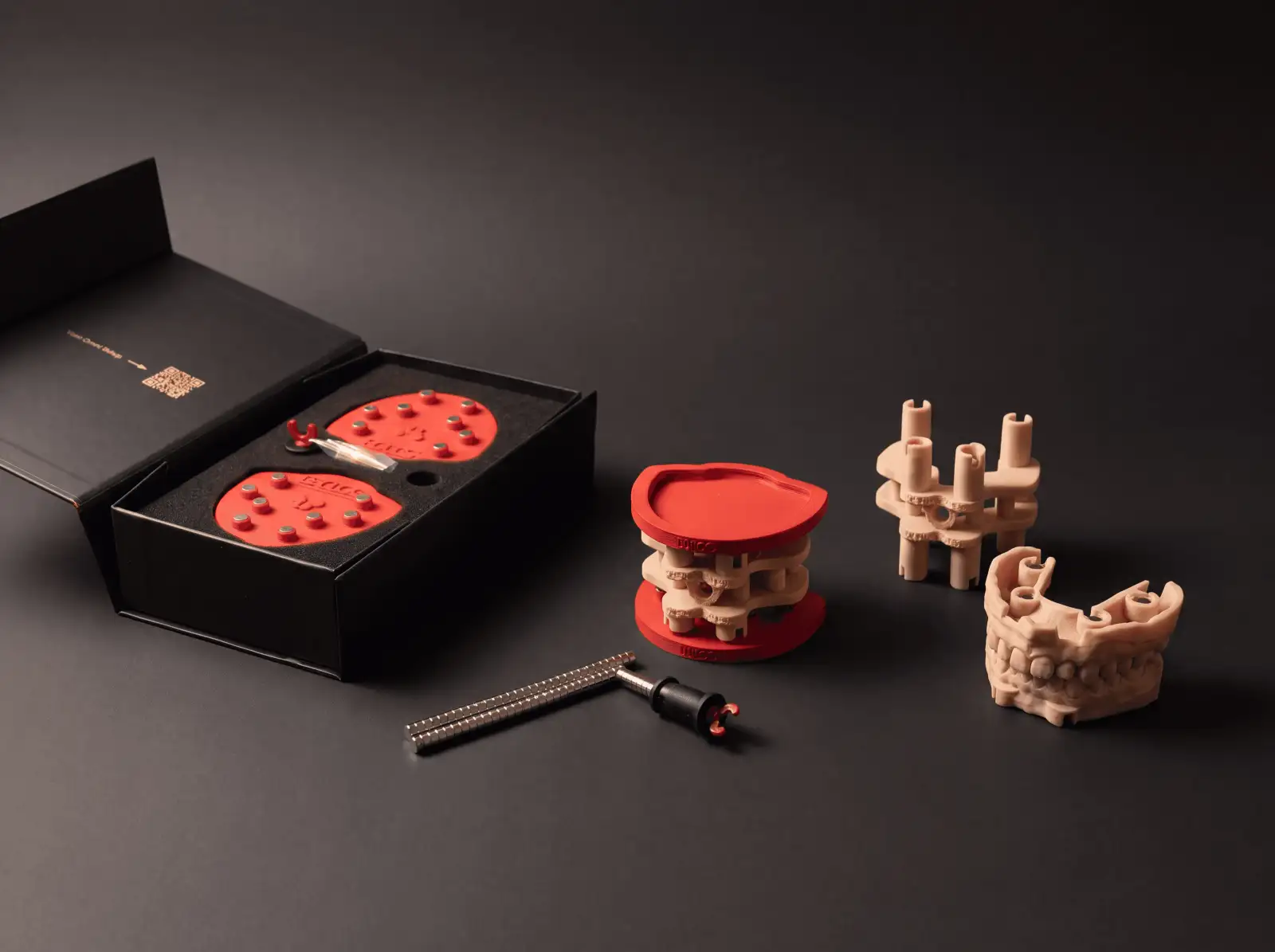 The DACOS Omni kit unboxed: red plates in the open box, the Omni GlueJet™ tool, a printed calibrator between two plates and printed models with magnet seats